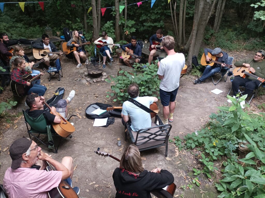 People playing guitar around a campfire during the day.